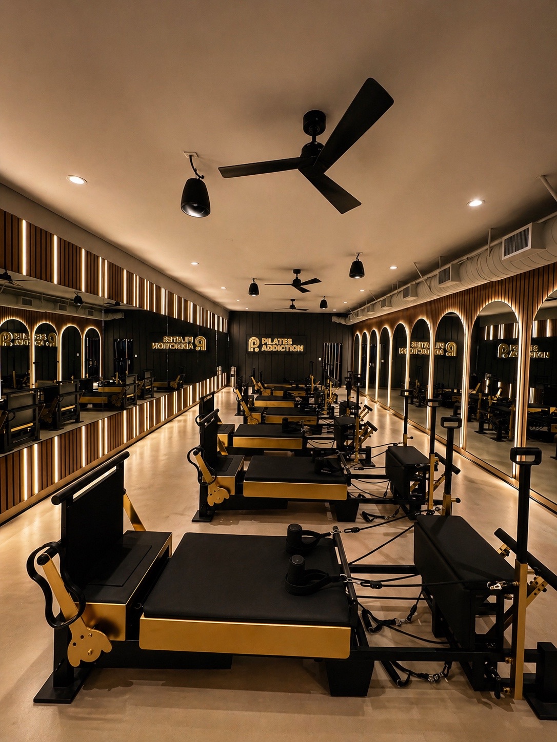 Pilates Addiction franchise studio with reformers, backlit arched mirrors and LED-lit wood slat walls