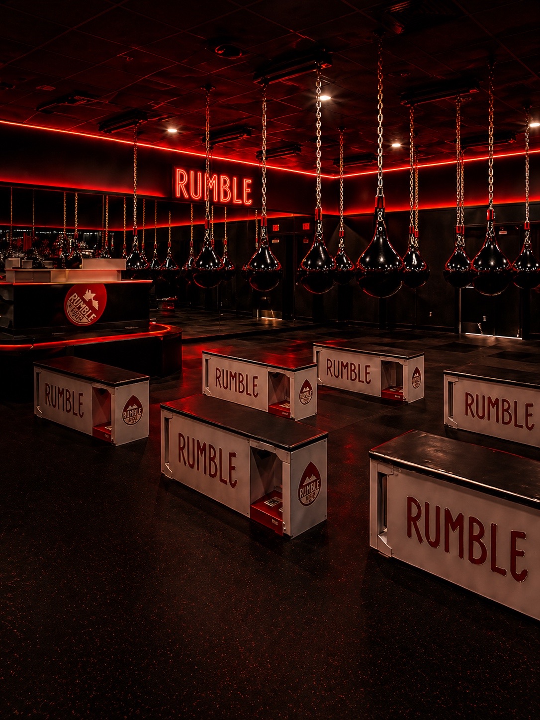 Rumble Boxing franchise gym with red LED perimeter lighting above heavy bags and branded benches